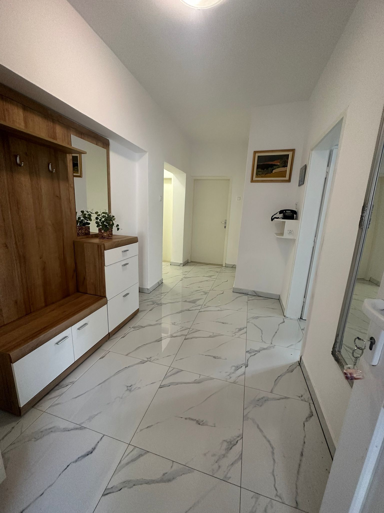 A hallway with a wooden bench, a white dresser, and a marble floor.