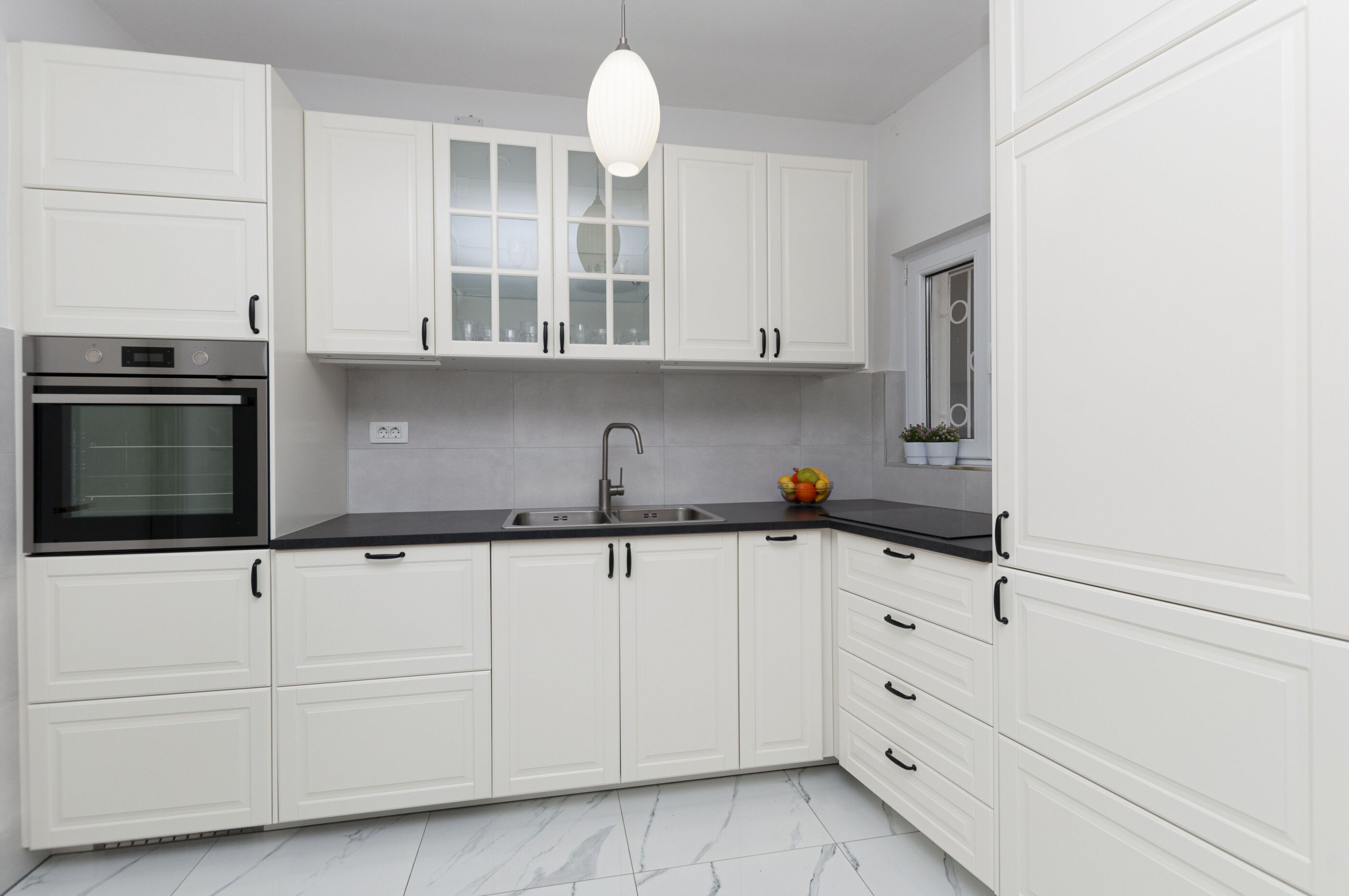 A modern kitchen with white cabinetry, a stainless steel sink, and a built-in oven.