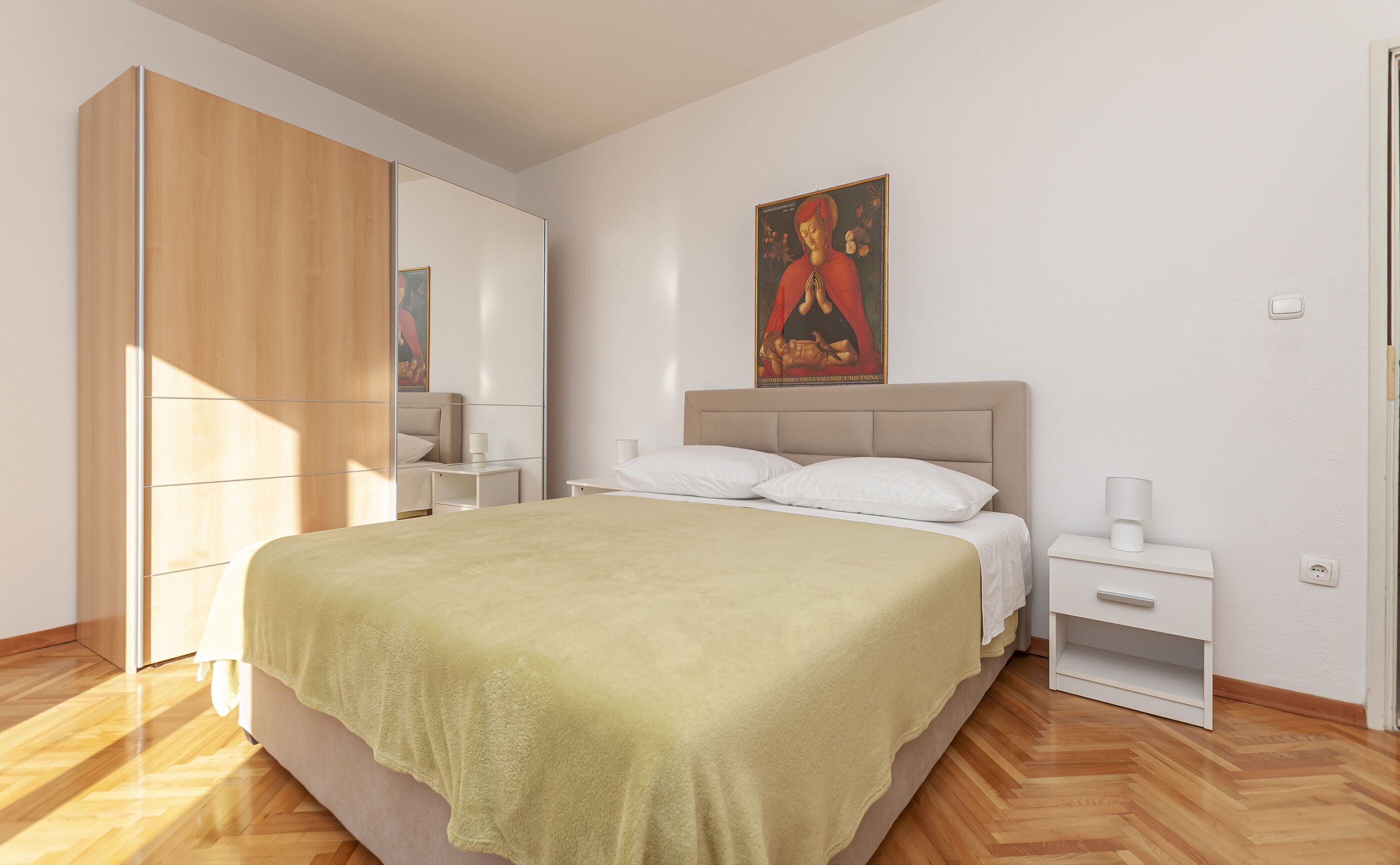 Un dormitorio con cama, mesitas de noche, un armario y un cuadro en la pared.