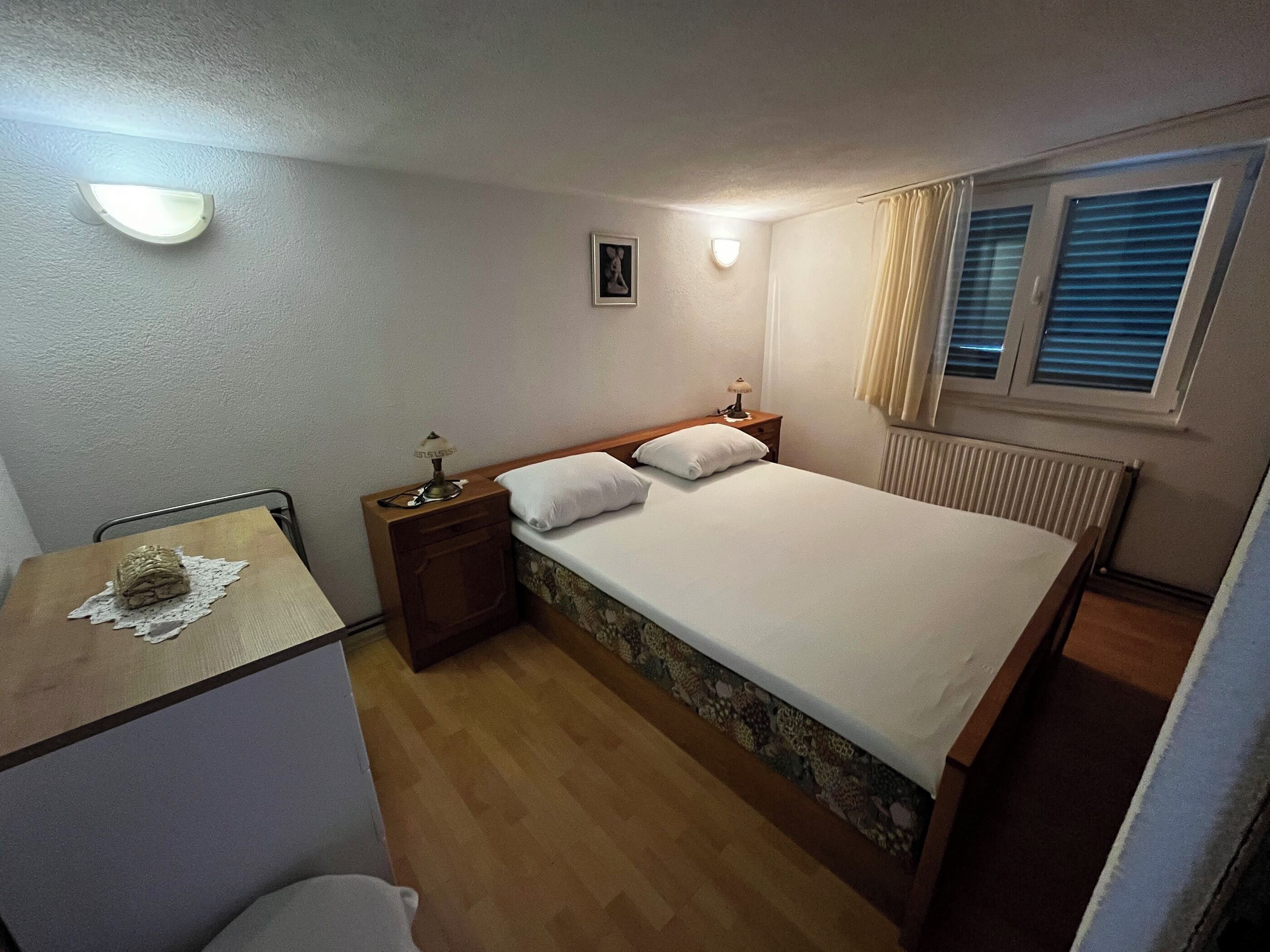 Une petite chambre à coucher, bien rangée, avec un lit simple, une table de chevet avec une lampe, une chaise et un radiateur.