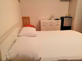 Un dormitorio con una cama, una silla de madera, un aparador y una mesita de noche con una lámpara.