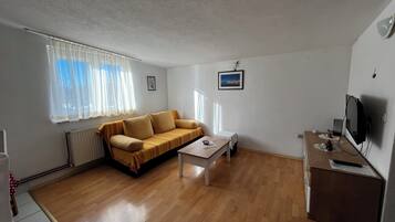 Una sala de estar pequeña y luminosa con un sofá, una mesita de centro y un televisor.
