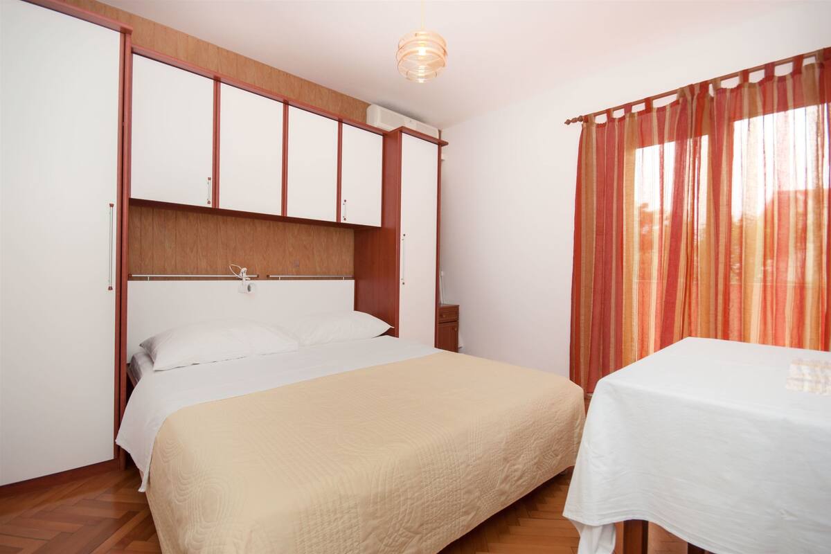 A bedroom with a bed, wooden wardrobe, and a table with a white tablecloth.