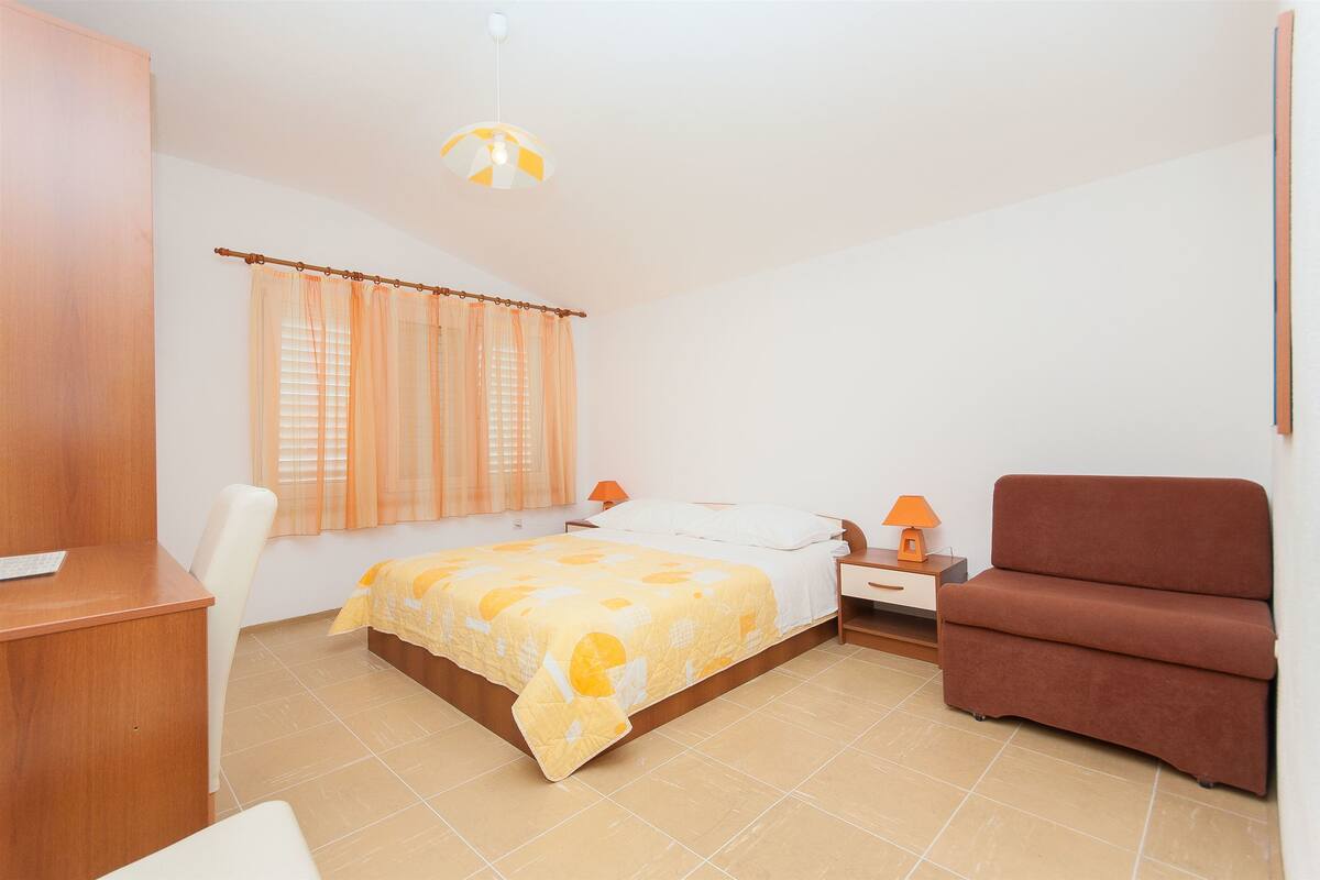 A bedroom with a bed, a desk, a chair, a nightstand, and a sofa.