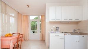 A compact kitchen with white cabinets, a sink, and a coffee maker. There is a dining table with chairs and a bowl of fruit. - Apartments Ante (Makarska)