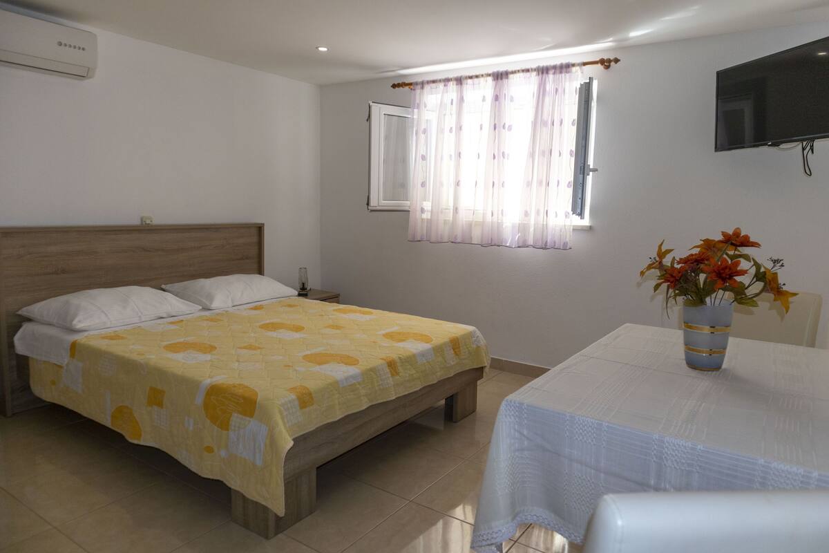 A bedroom with a bed, a bedside table, a TV mounted on the wall, and a window with curtains.