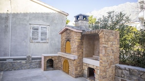 A stone-built outdoor kitchen area with a chimney, a stone wall, and a window with shutters. - Apartments Ante (Makarska)