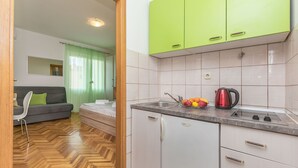 A compact kitchen with white cabinets and a green countertop, a sink, and a kettle. - Apartments and Room Nevenka (Makarska)
