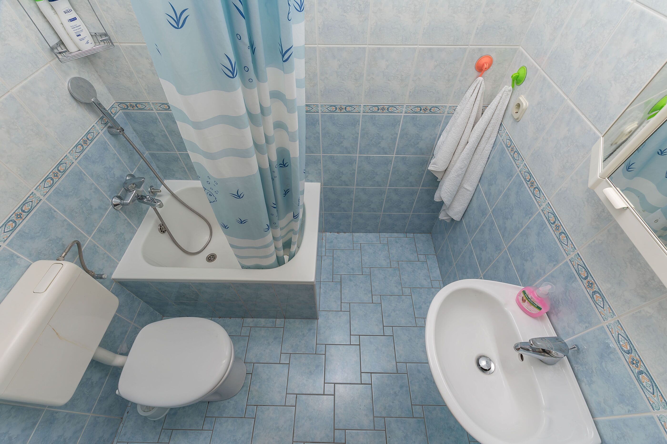 Casa de banho com chuveiro, sanita e lavatório, com azulejos azuis e cortina de chuveiro com padrão de ondas.