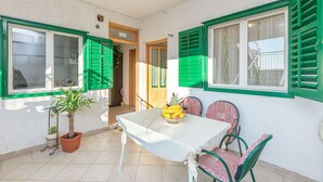 A small dining area with a table and chairs, a potted plant, and a window with green shutters. - Apartments and Room Nevenka (Makarska)
