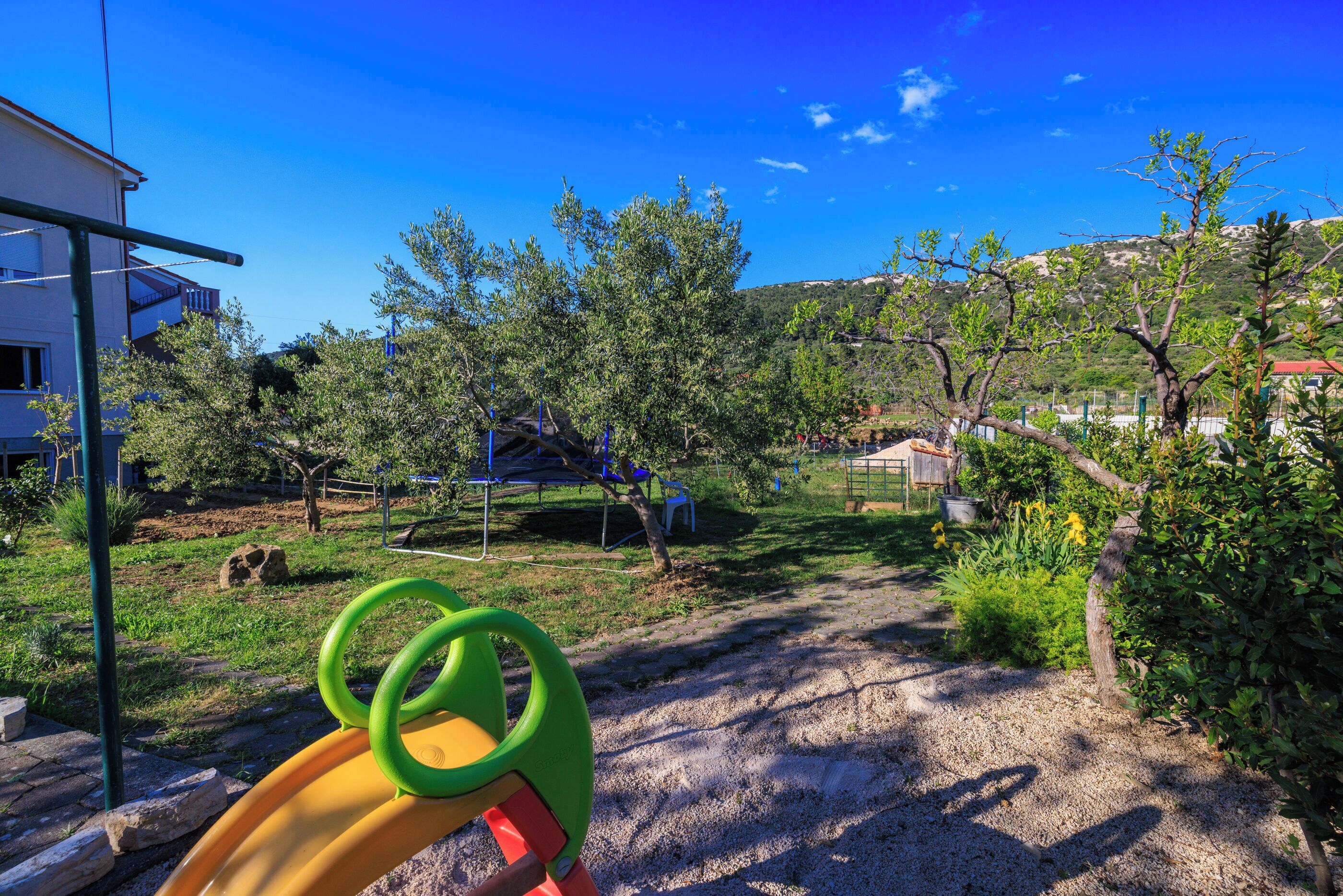 A playground with a slide, surrounded by trees and a building in the background.