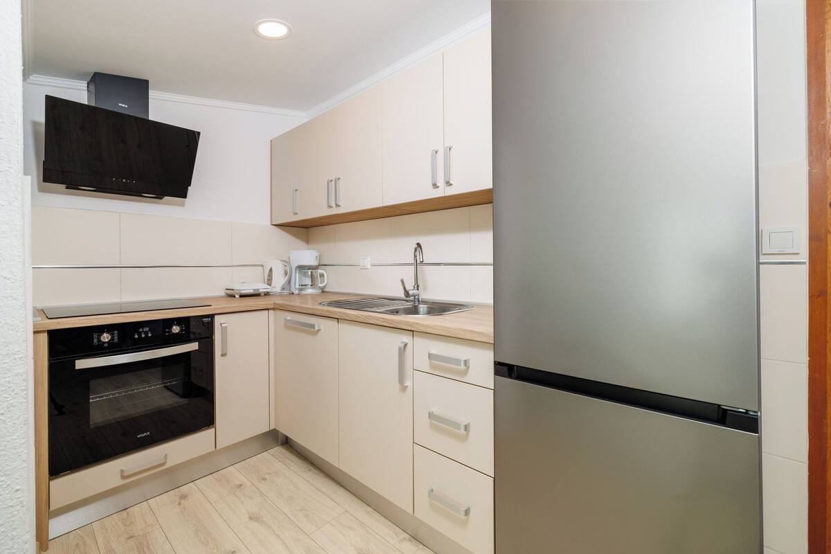 A modern kitchen with a built-in oven, a coffee maker, and a stainless steel refrigerator.