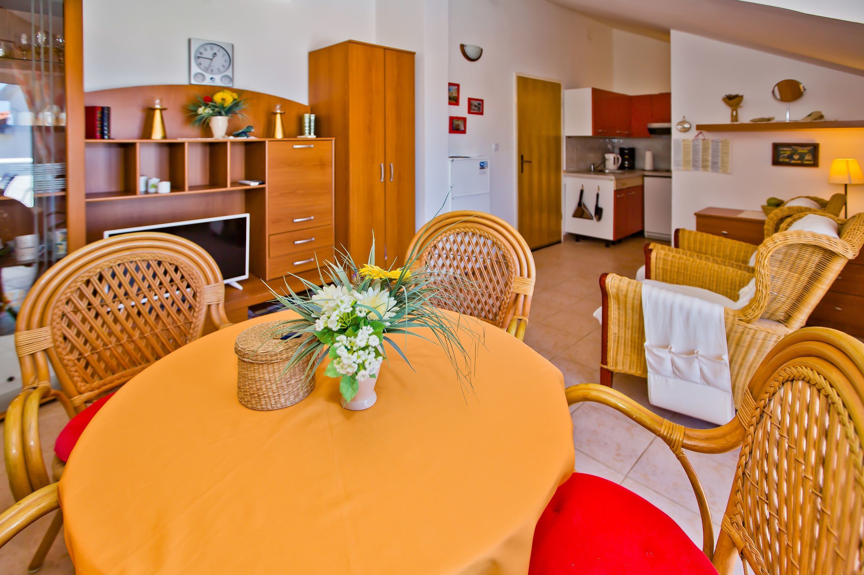 A dining area with wicker chairs, a round table, and a vase of flowers.