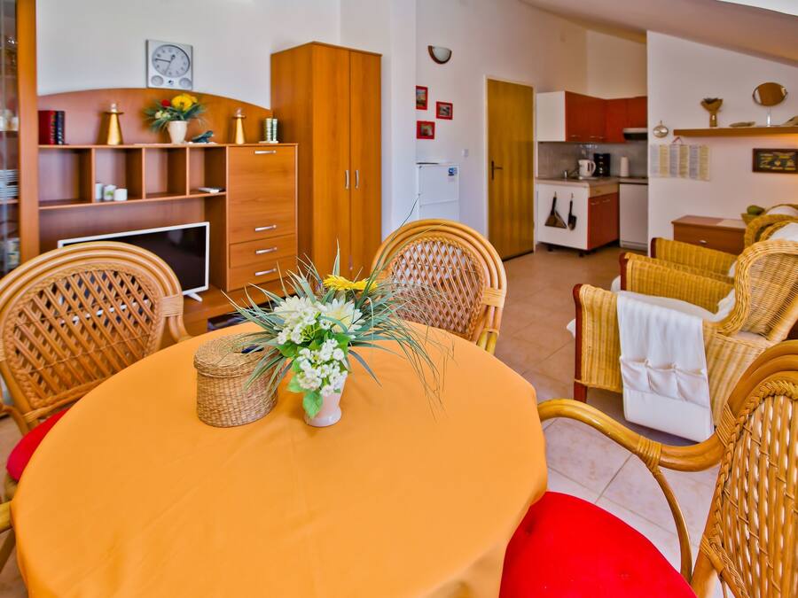 A dining area with wicker chairs, a round table, and a vase of flowers.