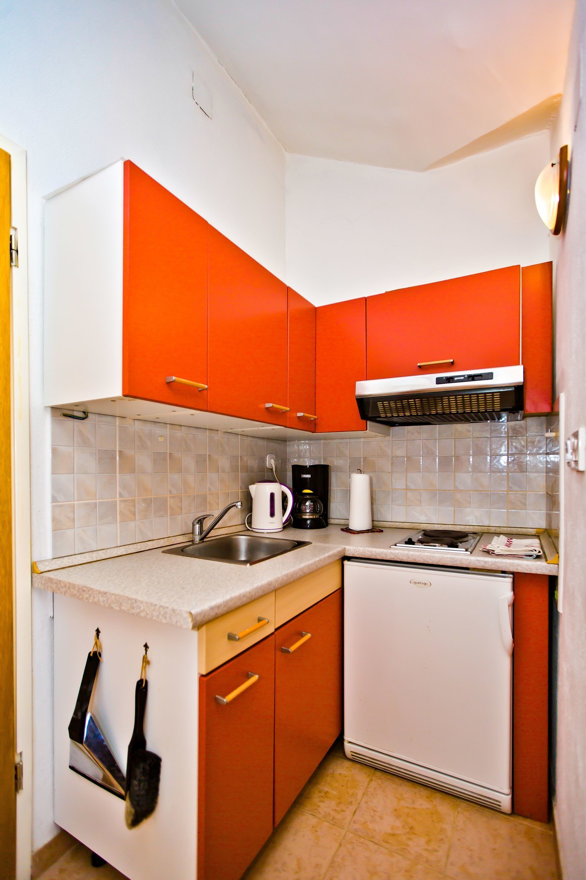 A compact kitchen with white and orange cabinets, a white dishwasher, and a coffee maker on the countertop.