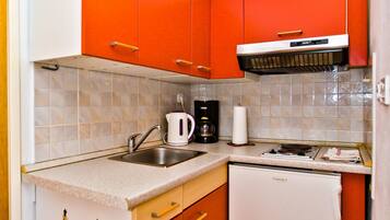 A compact kitchen with white and orange cabinets, a white dishwasher, and a coffee maker on the countertop.