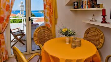 Un comedor con sillas de mimbre, una mesa redonda con mantel amarillo, una planta en maceta y vistas al mar a través de un ventanal.