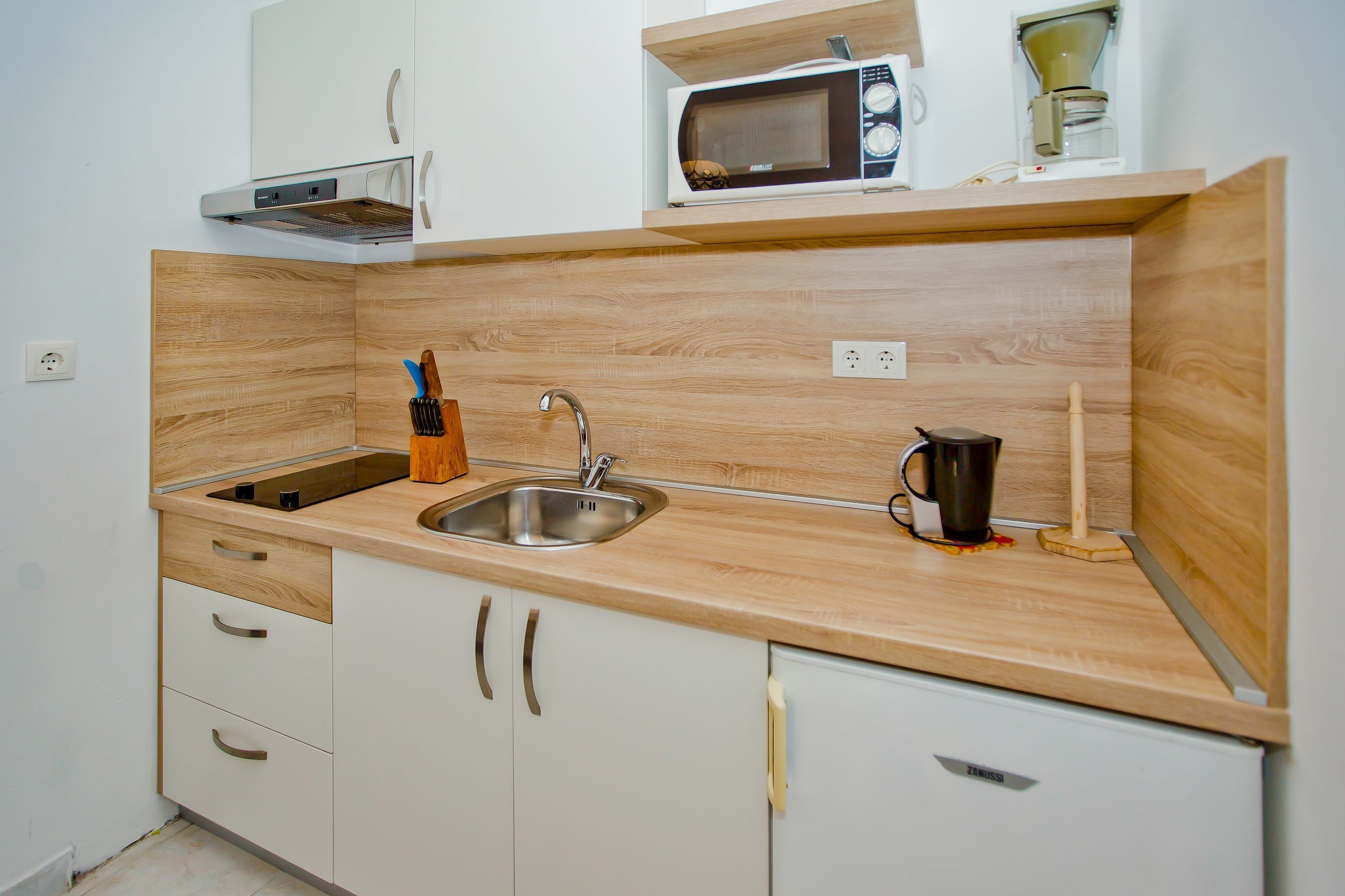 A kitchen with a wooden countertop, a stainless steel sink, a microwave, and a coffee maker.