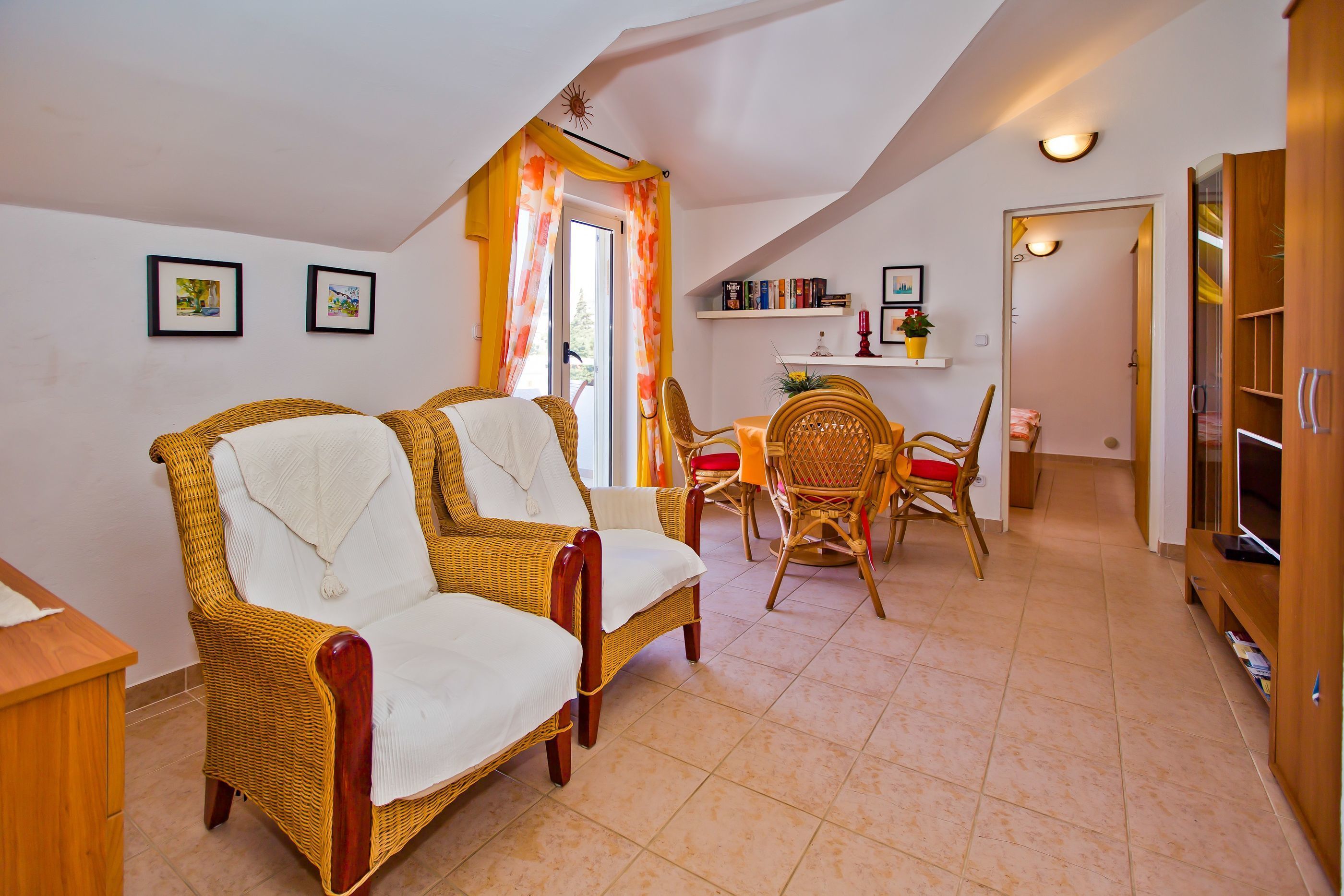 Una sala acogedora con muebles de mimbre, un comedor con sillas y una estantería.