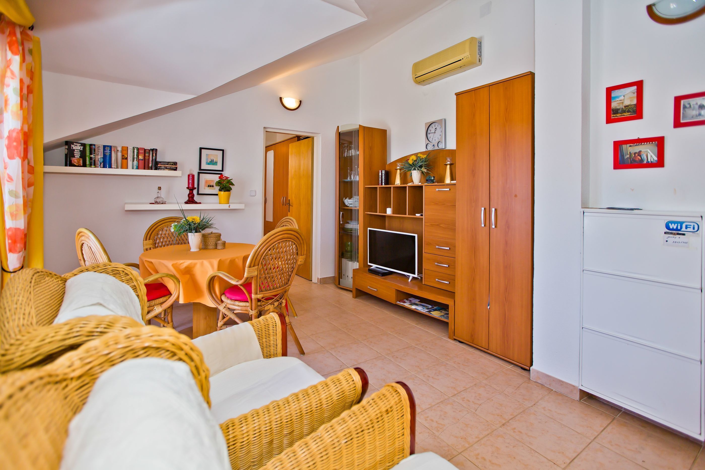A cozy living room with a dining table, wicker furniture, a TV, and a white refrigerator.