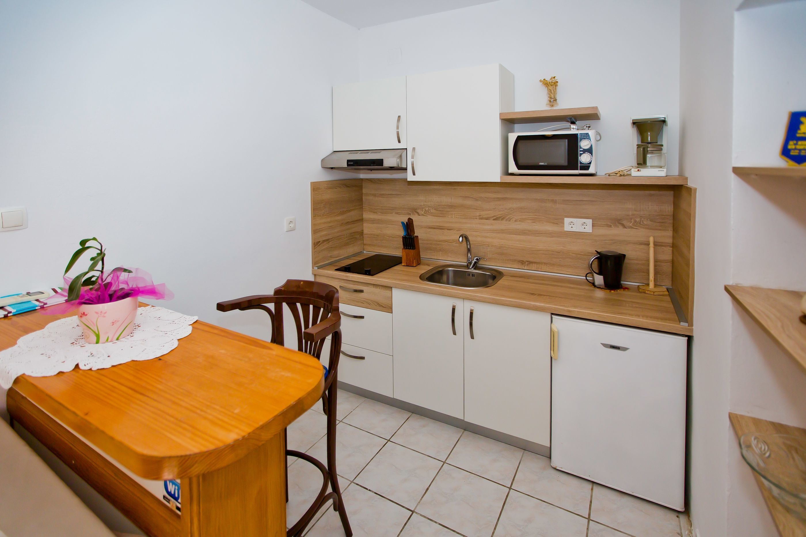 Cocina compacta con encimera de madera, armarios blancos, microondas, cafetera y fregadero.