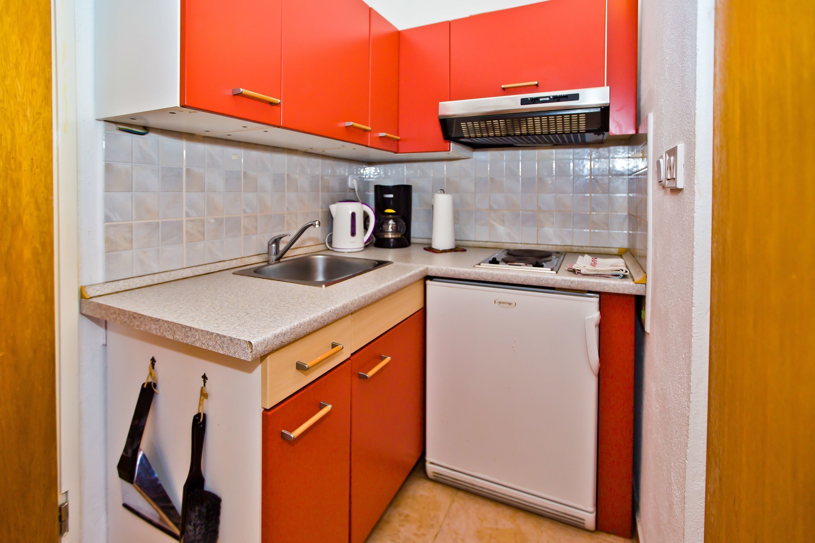 A compact kitchen with red cabinets, a white dishwasher, and a stainless steel sink.