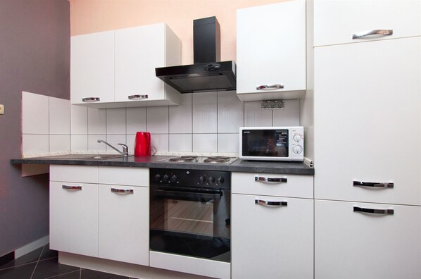 A modern kitchen with white cabinets, a black stove, a red kettle, and a microwave. - Apartments Martina (Marina)