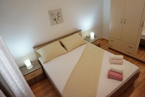 A neatly made bed with pillows and a blanket, a bedside table with a lamp, and a wardrobe. - Apartment Summer Day (Vodice)