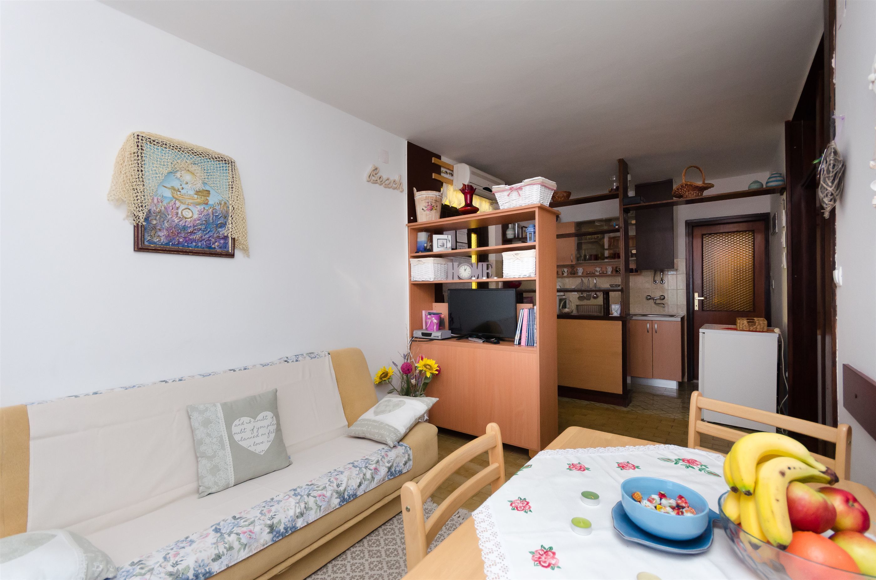 Una sala de estar acogedora con un sofá, una mesa de comedor con fruta, y una zona de cocina al fondo.