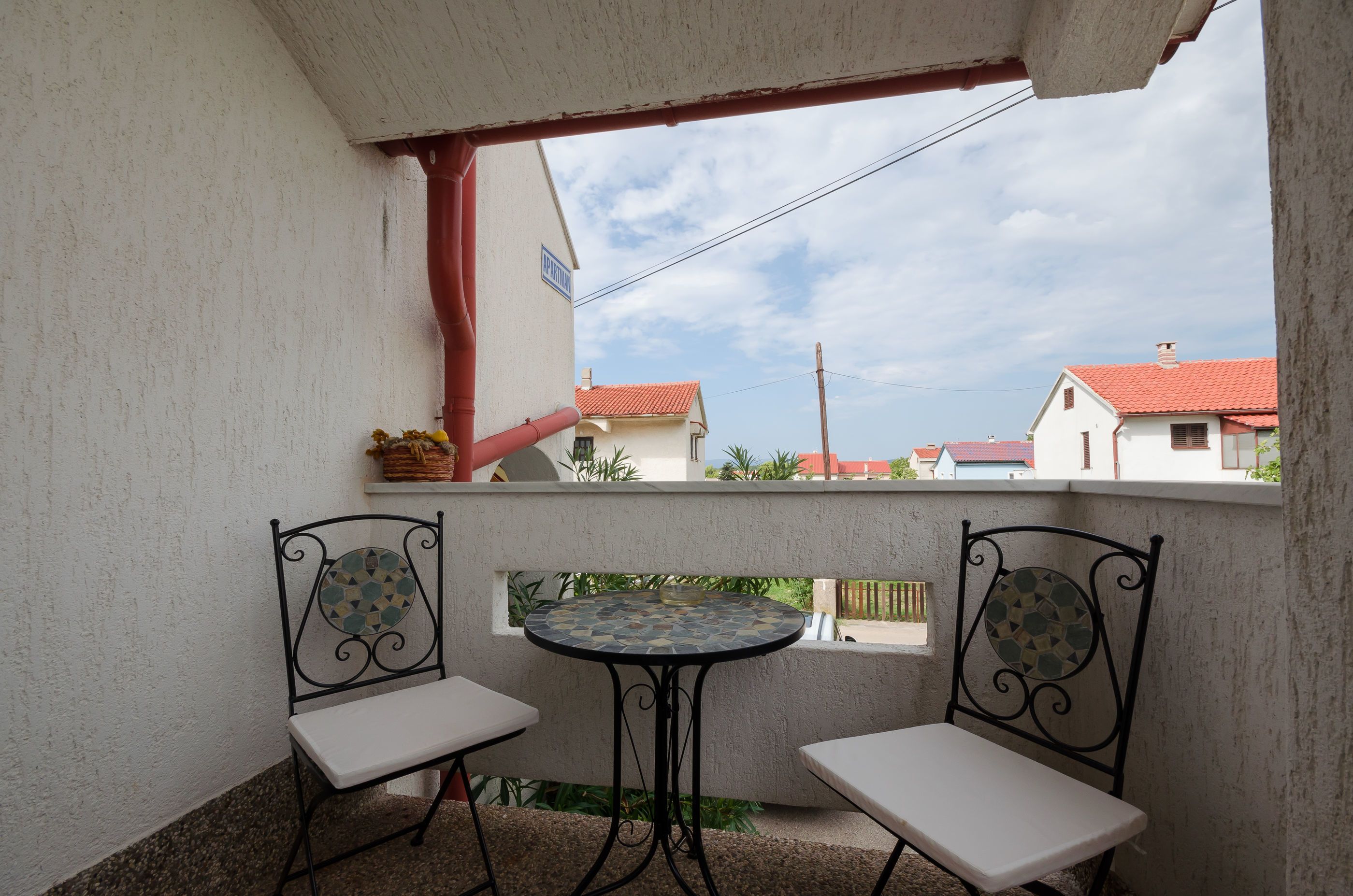 A balcony with two chairs and a small table, overlooking a residential area with houses and a clear sky.