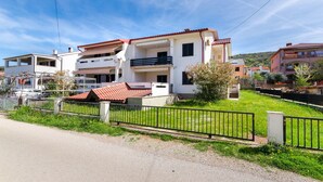 A two-story residential building with a red-tiled roof, a balcony, and a small garden area. - Apartments Branka (Punat)