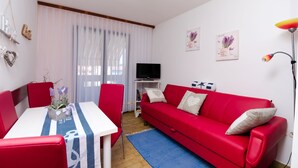 A living room with a red sofa, a TV stand, and a dining table with chairs. - Apartments Branka (Punat)