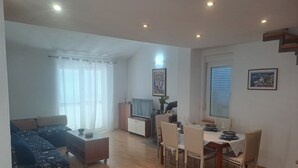 Una sala de estar con un sofá, una mesa de comedor con sillas, un televisor y una ventana con persianas.