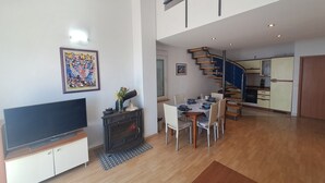 Una sala moderna con televisión de pantalla plana, chimenea, comedor, escalera y cocina.