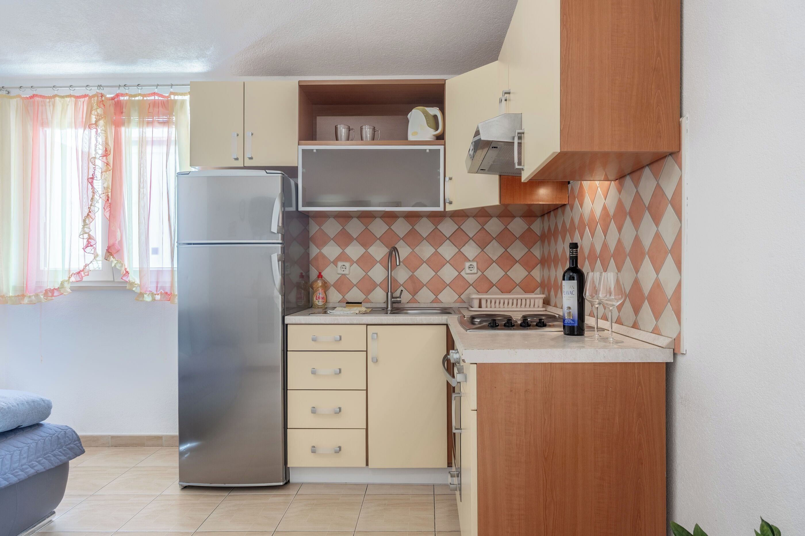 A compact kitchen with a refrigerator, a sink, and a countertop with a bottle and glass.