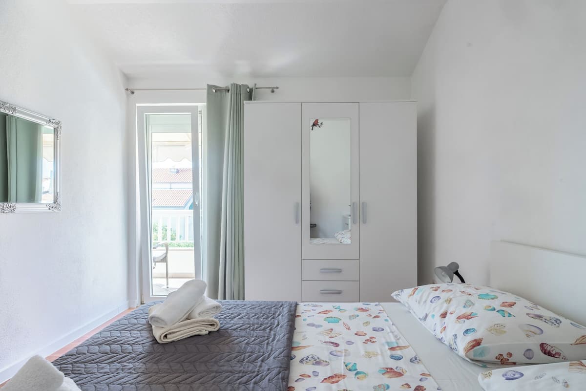 Ein Schlafzimmer mit Bett, Kleiderschrank, Spiegel und einem Fenster mit Vorhängen.