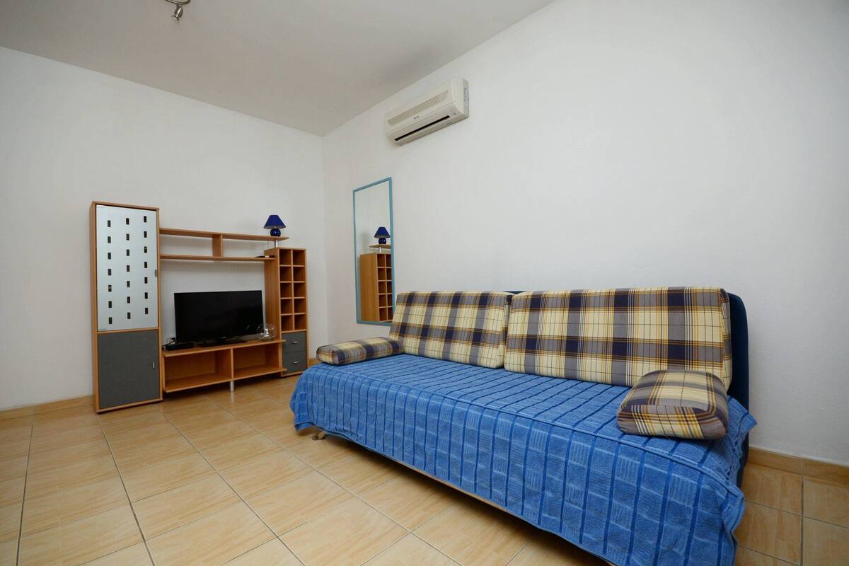 Ein Zimmer mit einem blauen Sofa, einem Fernseher, einem Spiegel und einem Holzkasten.