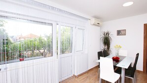 A dining area with a table and chairs, a potted plant, and a window with sheer curtains. - Apartment Anica (Trogir)