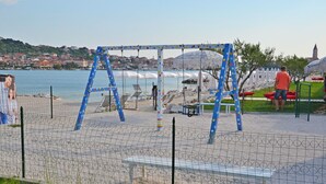 A beachside park with a swing set, lounge chairs, and umbrellas. - Apartment Anica (Trogir)