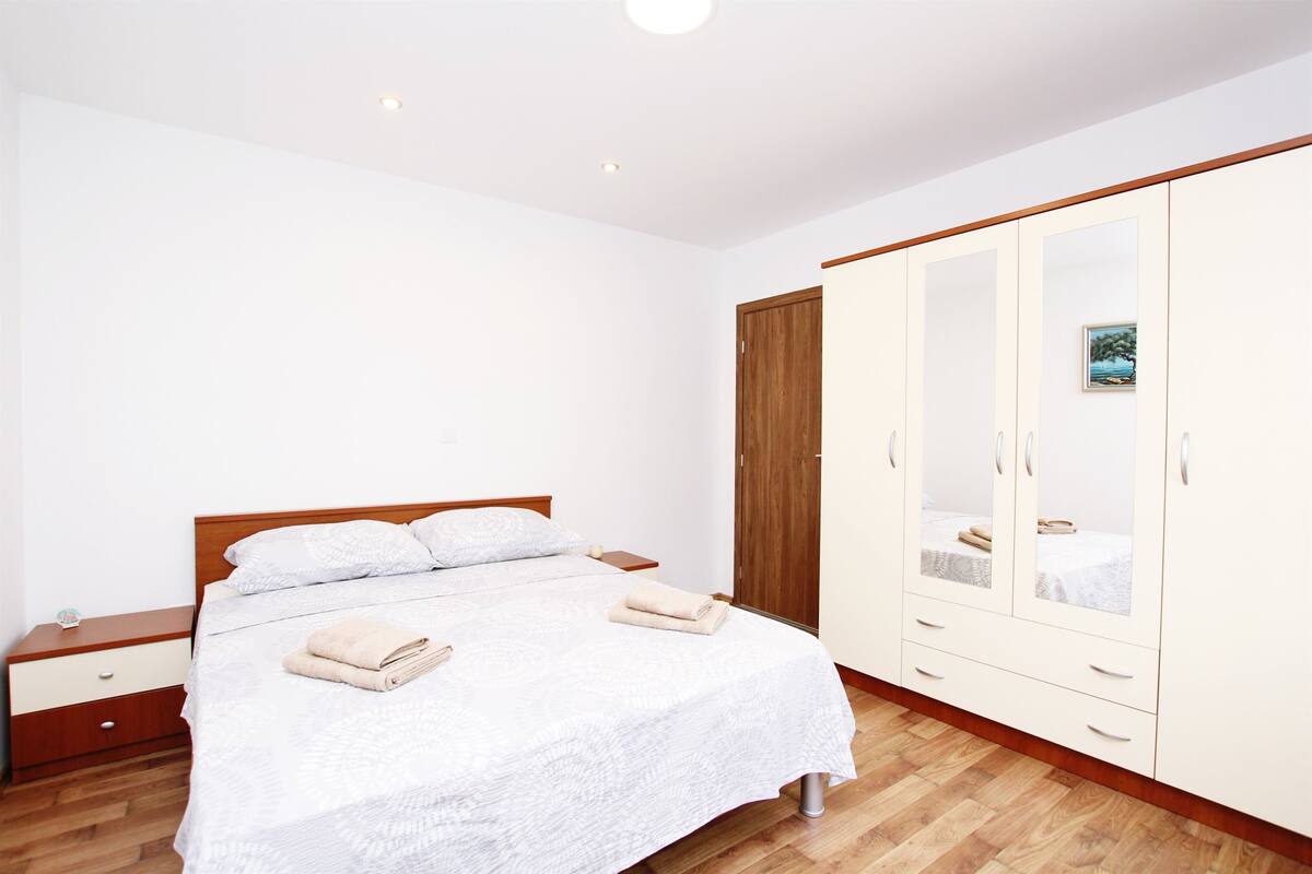 Ein Schlafzimmer mit einem Bett, einem Nachttisch aus Holz, einem Kleiderschrank und einem kleinen Beistelltisch.