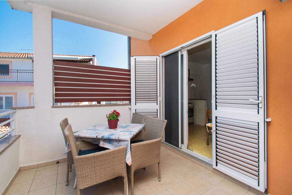 A balcony with a table and chairs, a sliding door, and a view of a building in the background.
