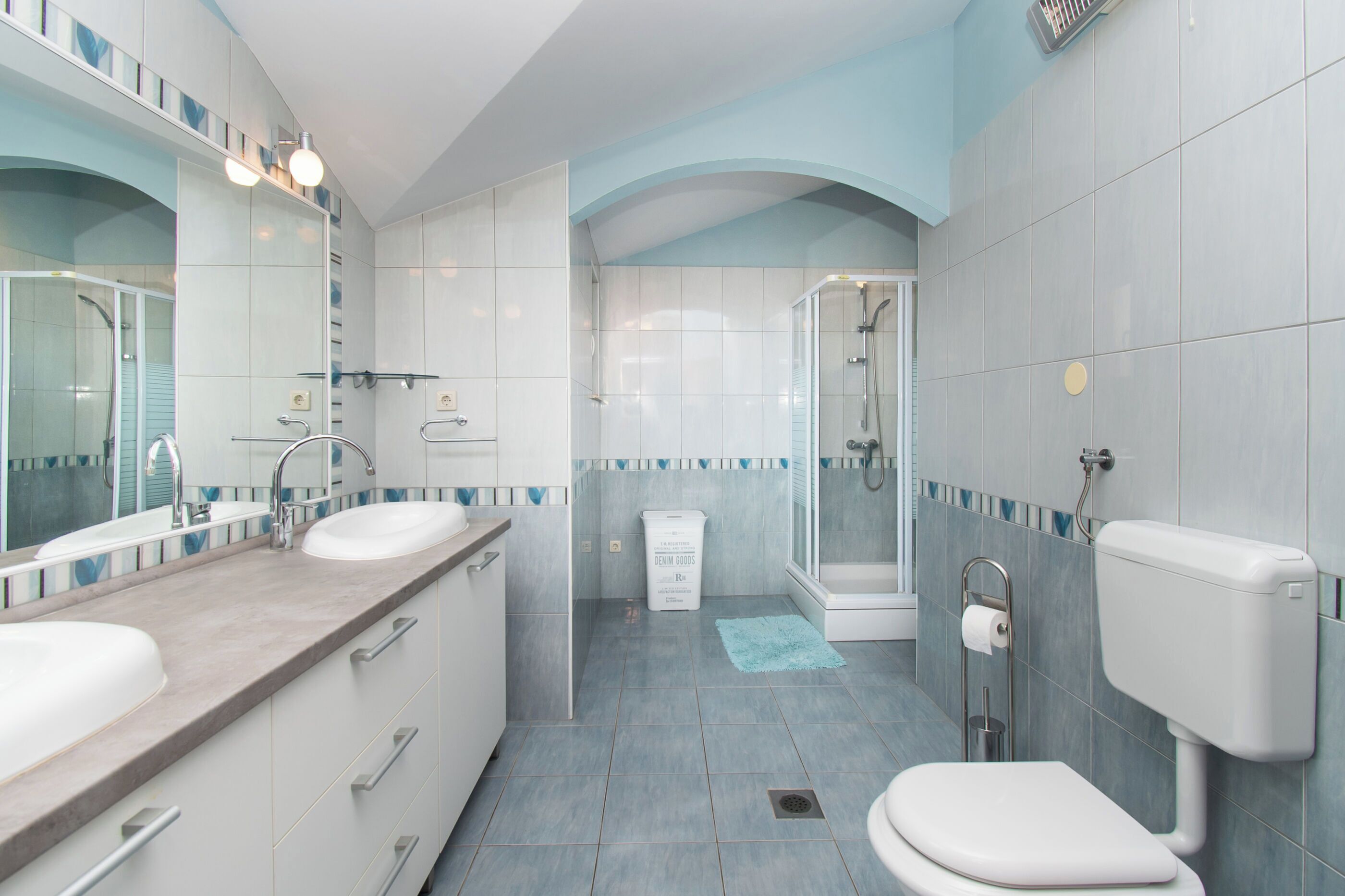 Ein modernes Badezimmer mit zwei Waschbecken, einer Toilette, einer Dusche und einem großen Spiegel.