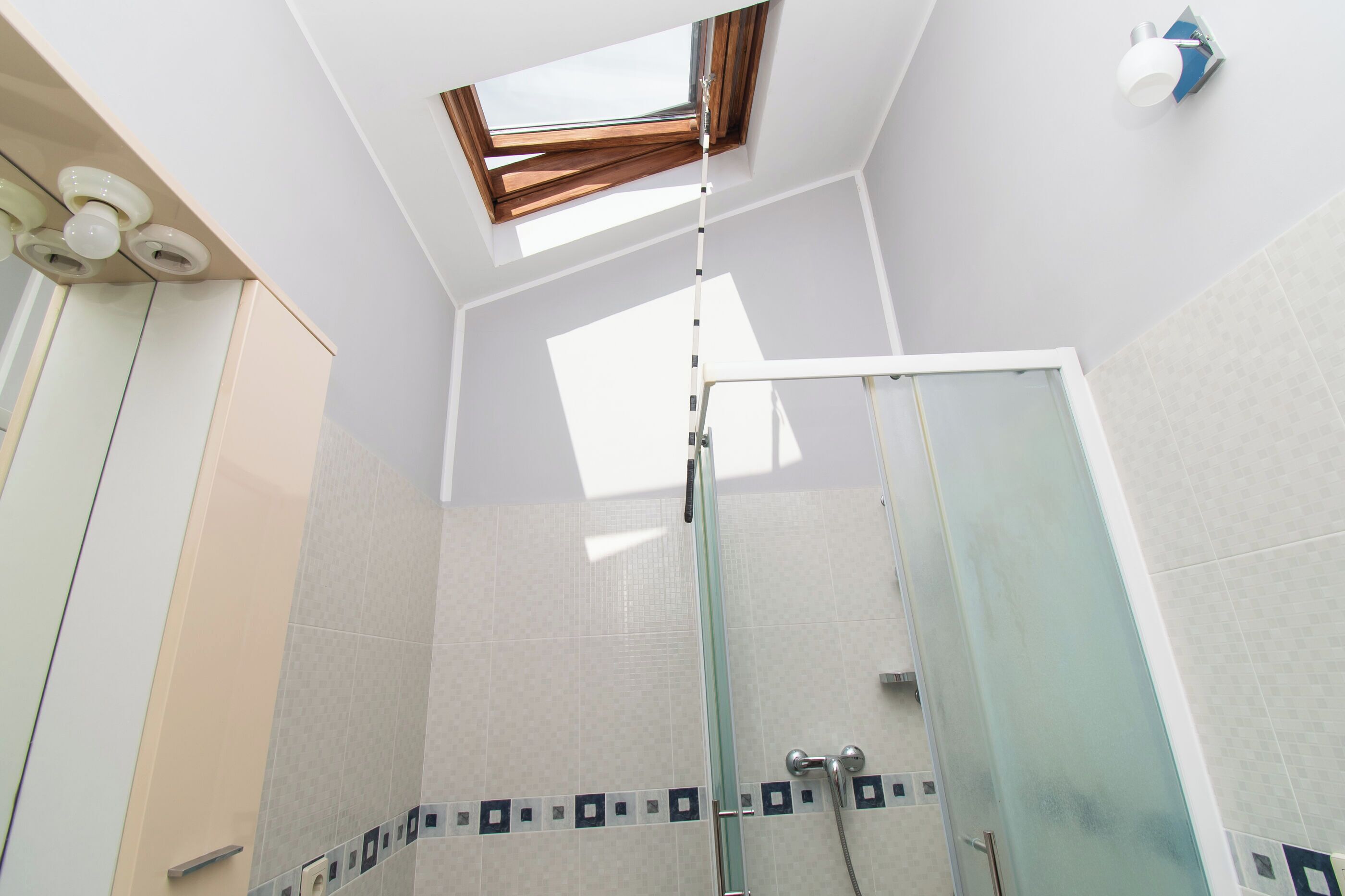 A modern bathroom with a skylight, a glass shower enclosure, and a tiled floor.