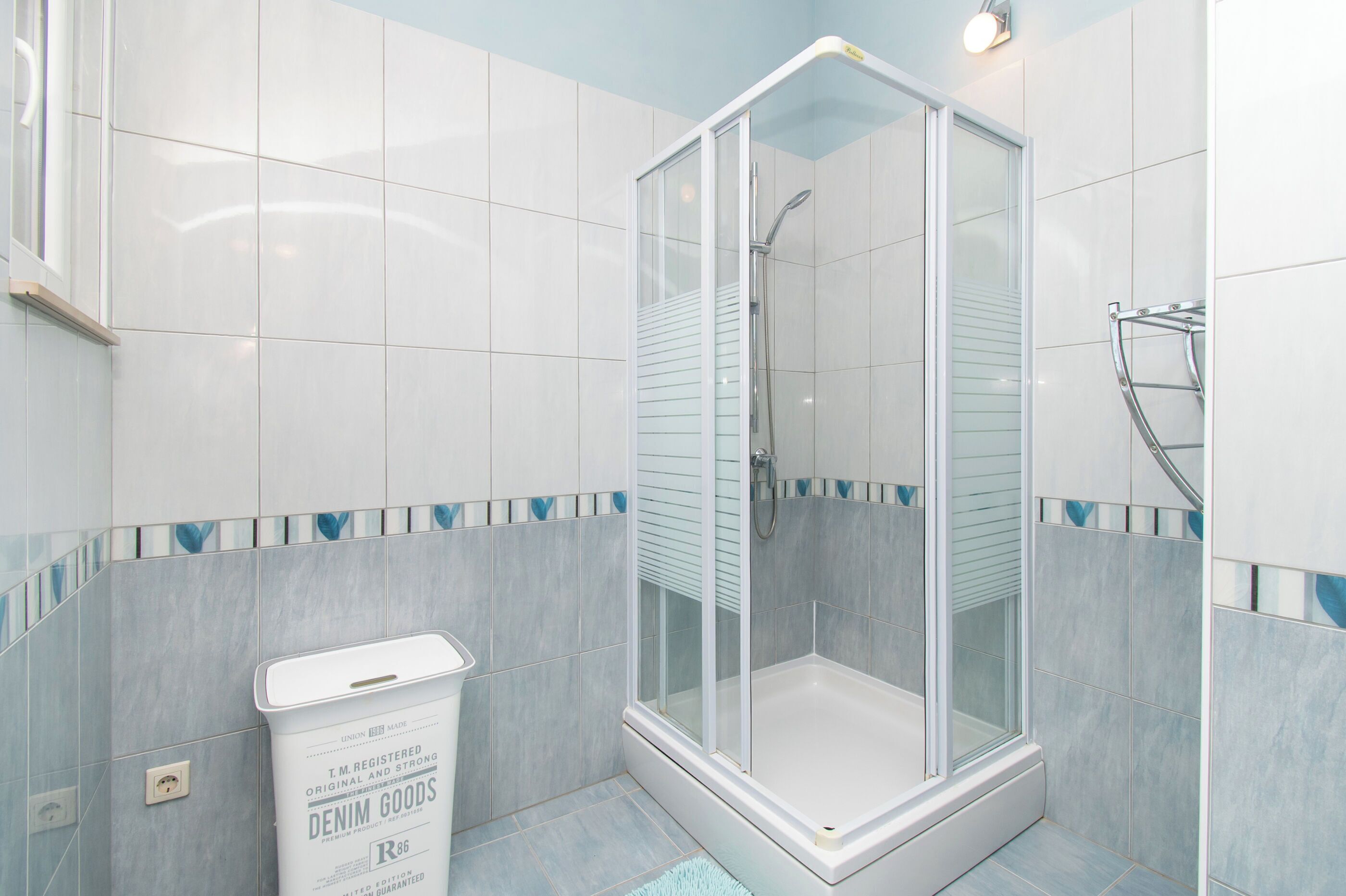 Une salle de bain moderne avec une douche à parois de verre, des carreaux blancs et une bordure décorative bleue.
