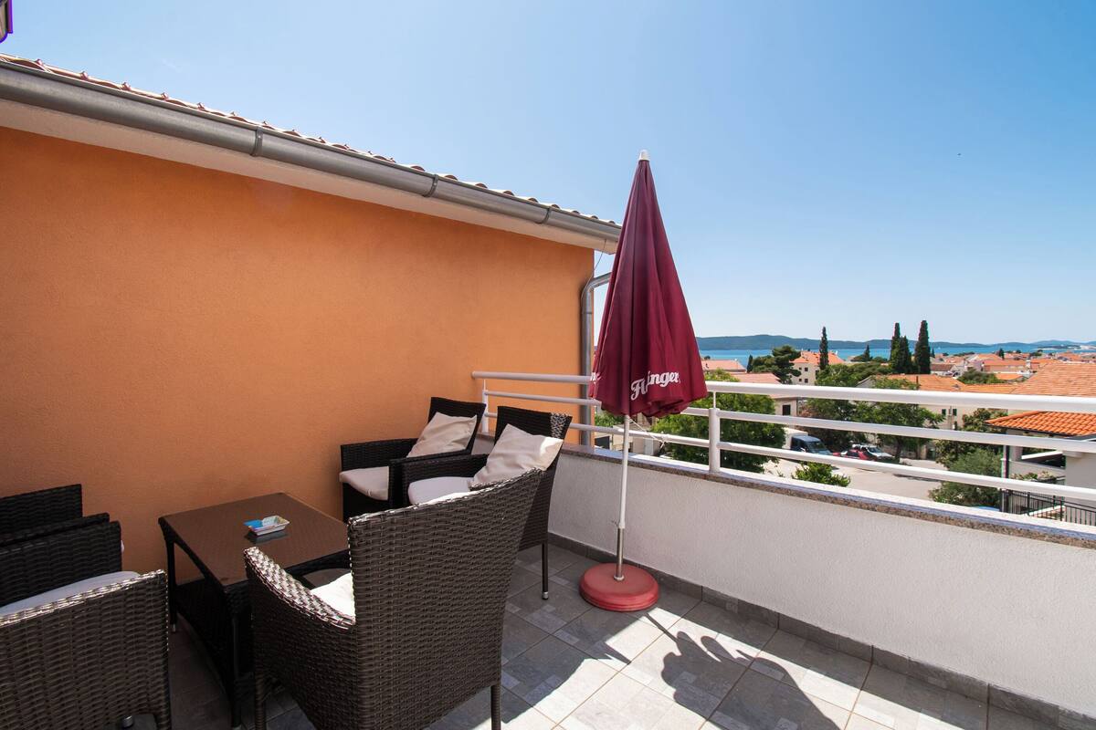 A balcony with wicker furniture, a table, and a red umbrella.
