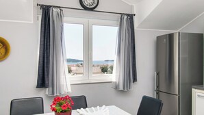 A dining area with a table, chairs, a vase with flowers, a decorative bowl, and a view of the sea through a window with curtains. - Apartments Cace (Brodarica)