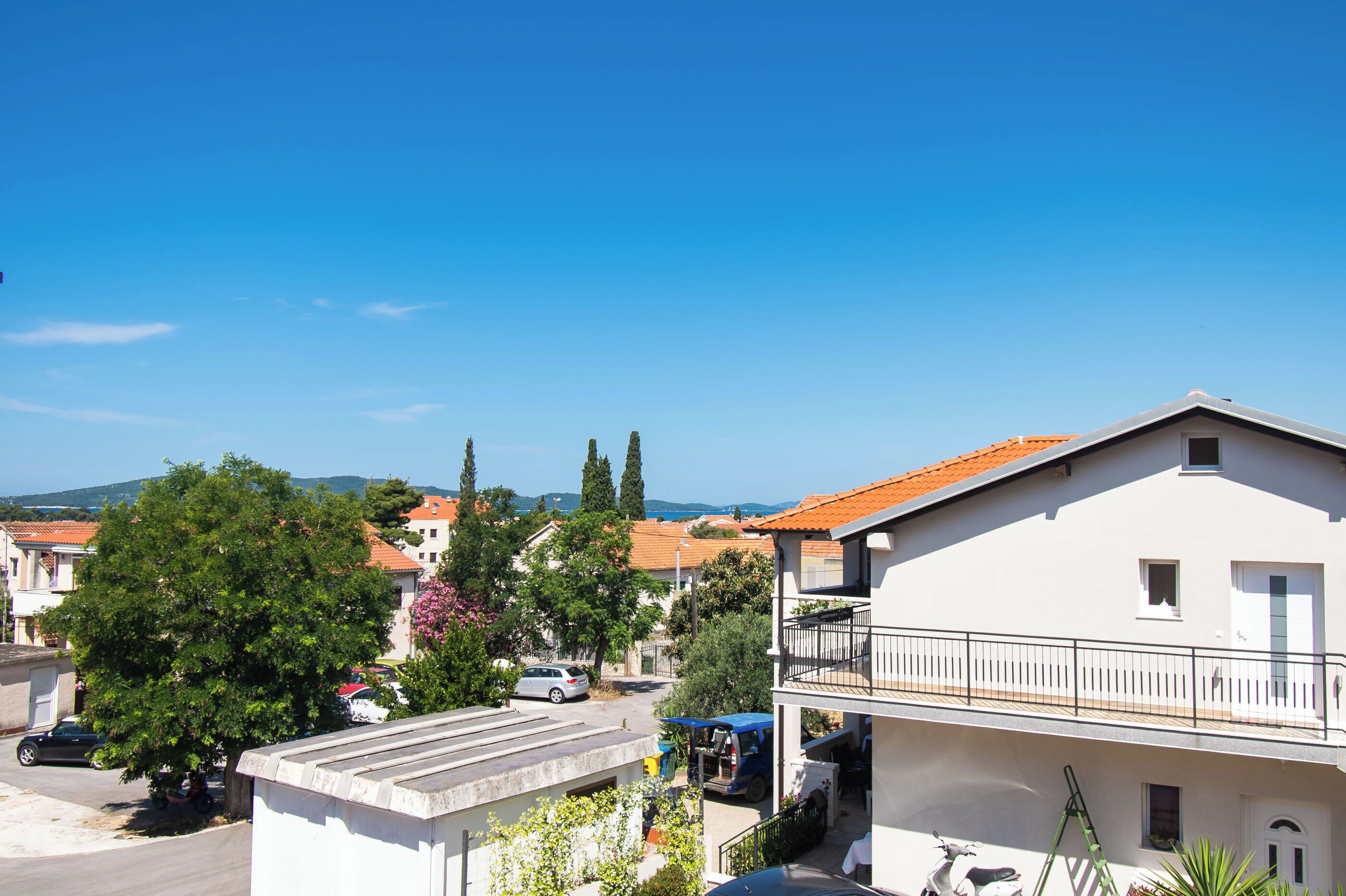 A residential area with a white building featuring a balcony and a red-tiled roof.