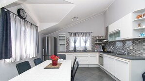 A modern kitchen with white cabinets, a black countertop, and a tiled backsplash. There is a dining table with chairs and a vase of red flowers. - Apartments Cace (Brodarica)