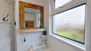 Un baño con un espejo de marco de madera, un lavamanos blanco y una ventana con vidrio esmerilado.