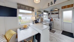 A compact kitchen with a dining area, a small refrigerator, and a window with blinds. - F17 Up-A-Bank, Riviere Towans (Hayle)